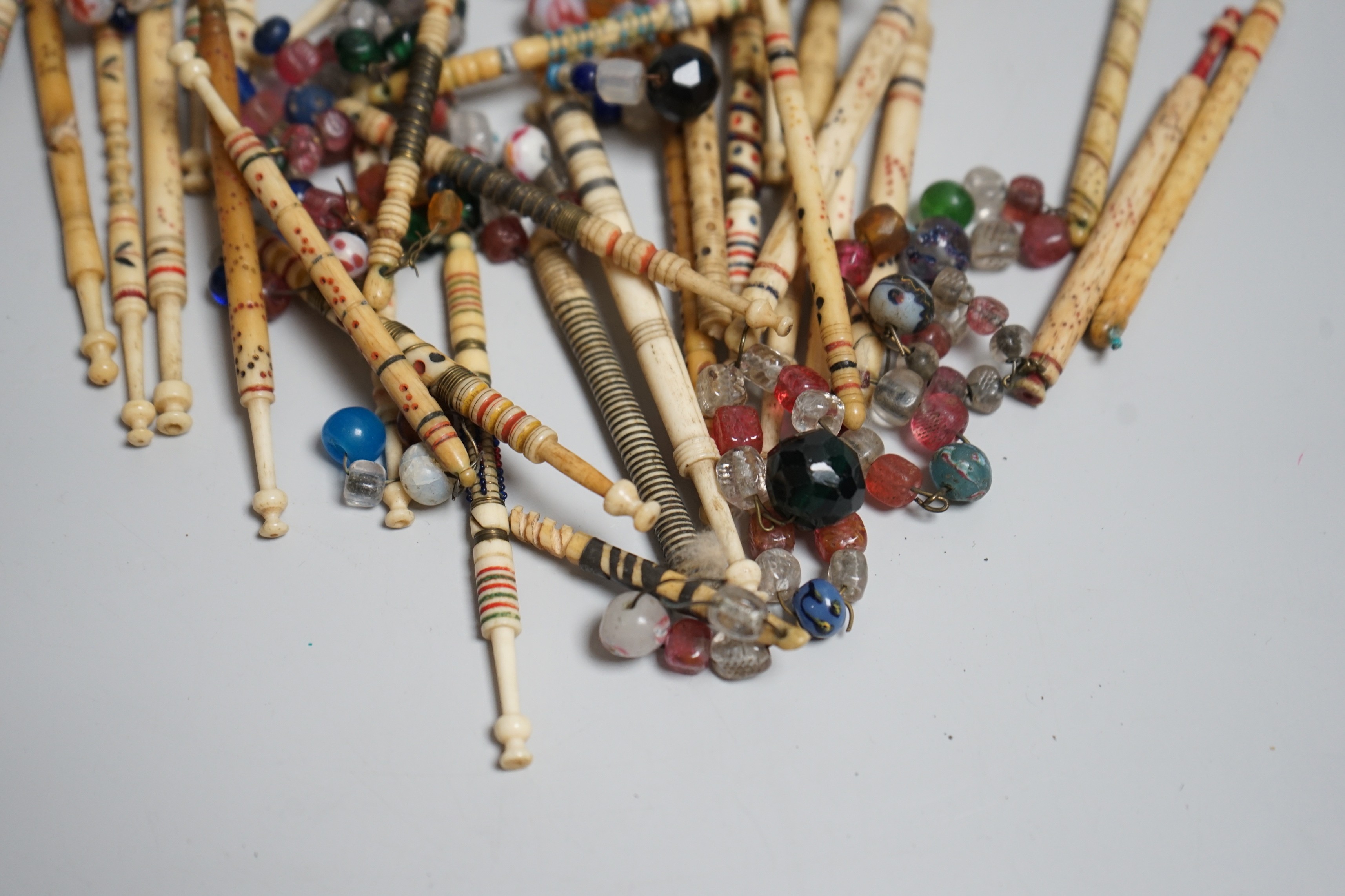 Twenty 19th century ornately decorated lace bobbins with glass bead tops and eleven carved bobbins with indistinctly carved surnames and names